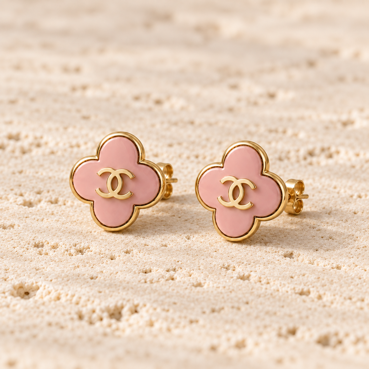 Second Soie vintage Chanel clover stud earrings in blush-pink enamel with gold-tone CC logo on a textured surface.