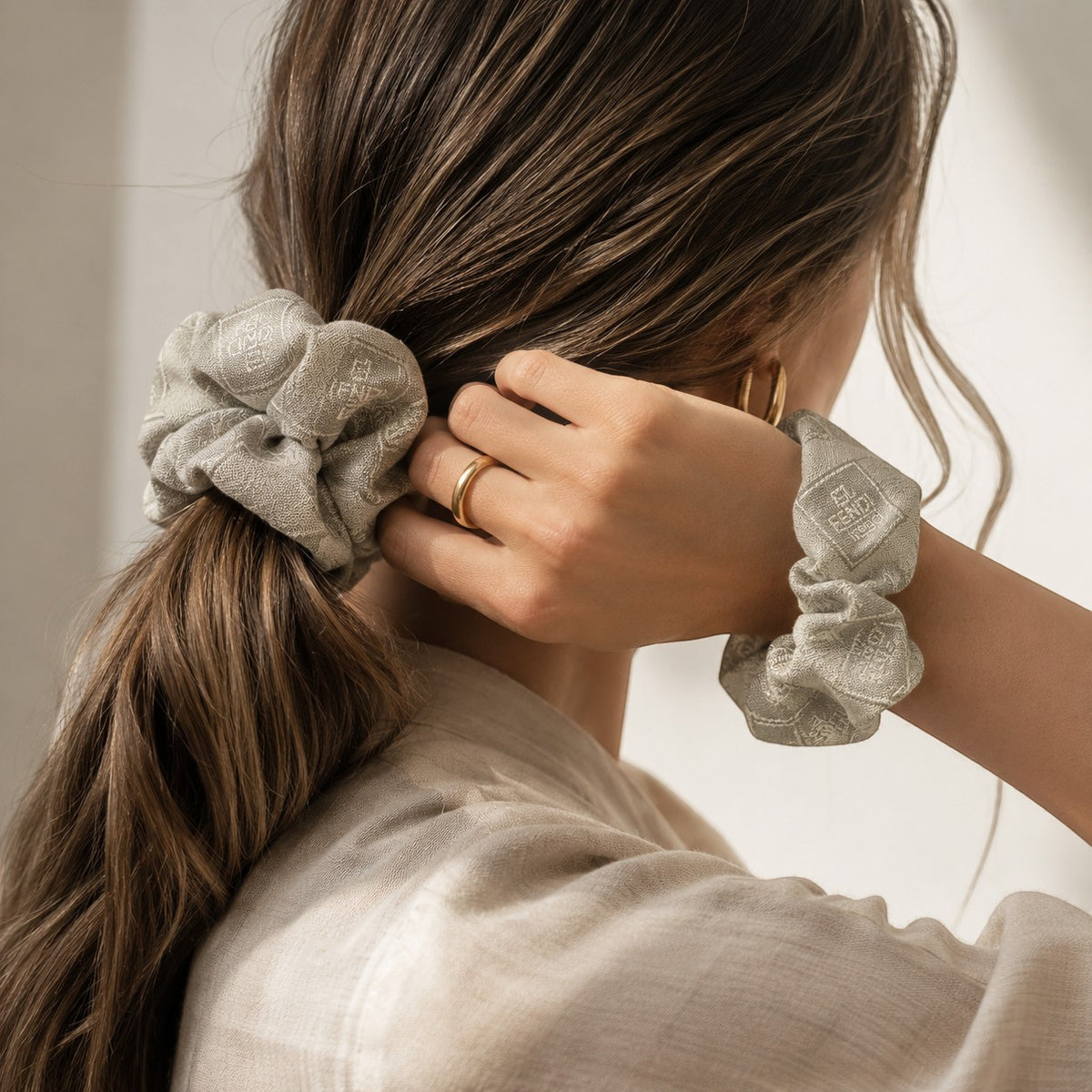 Second Soie sage gray Fendi monogram scrunchie worn in a ponytail and on the wrist, showing soft silk texture.