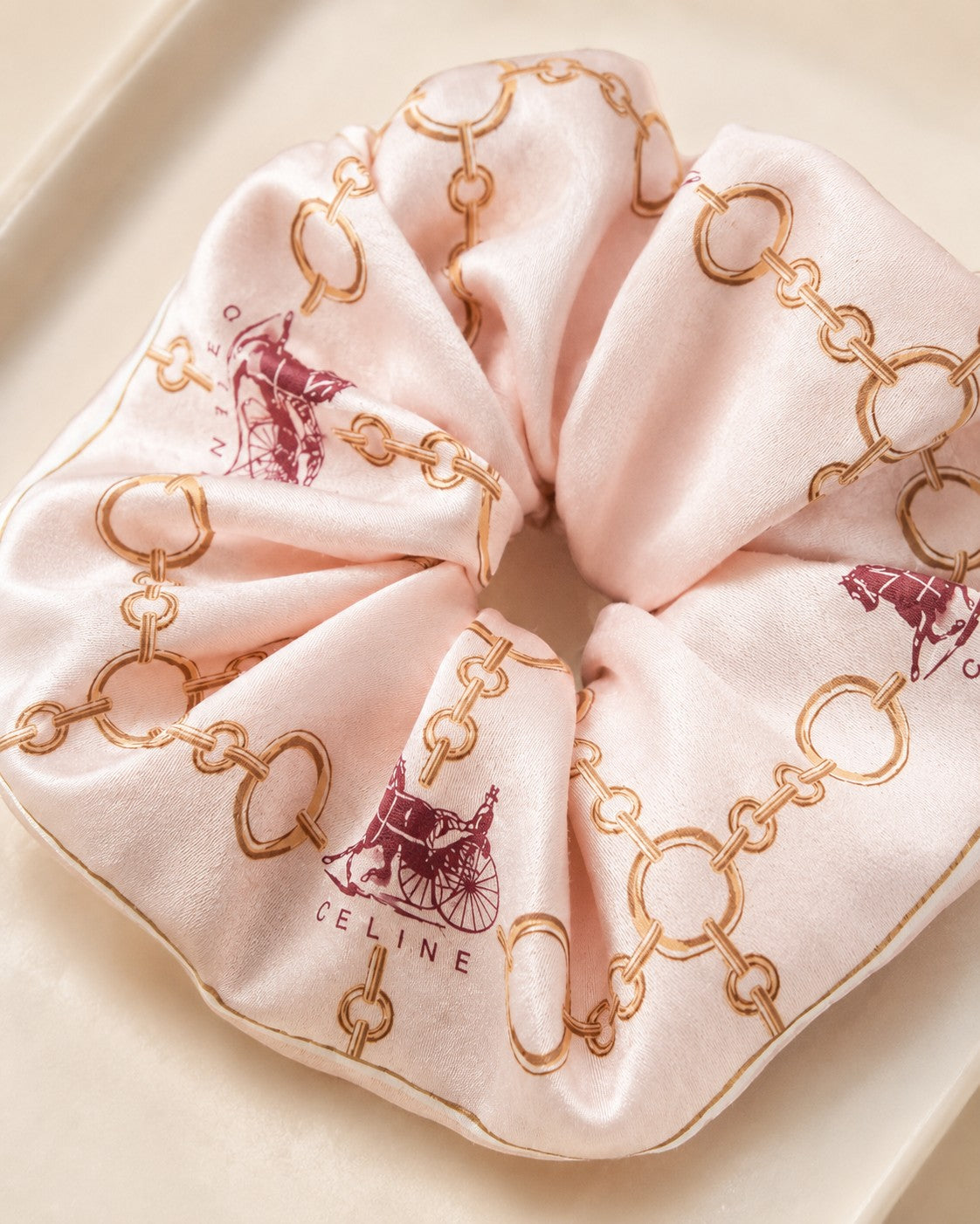 Second Soie jumbo silk scrunchie in blush with a Celine equestrian print featuring gold chains and burgundy carriages.