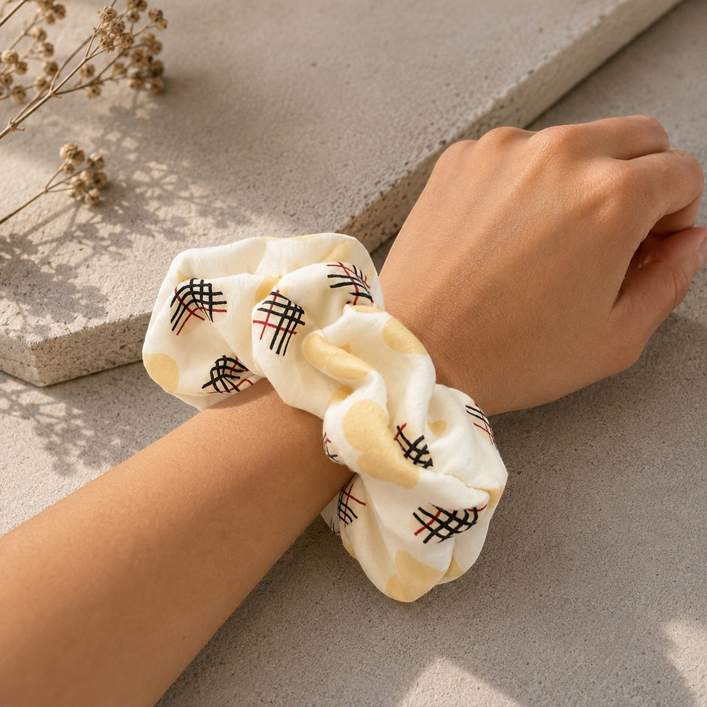 Second Soie jumbo scrunchie in cream fabric with heart and check pattern worn on a wrist against a stone background