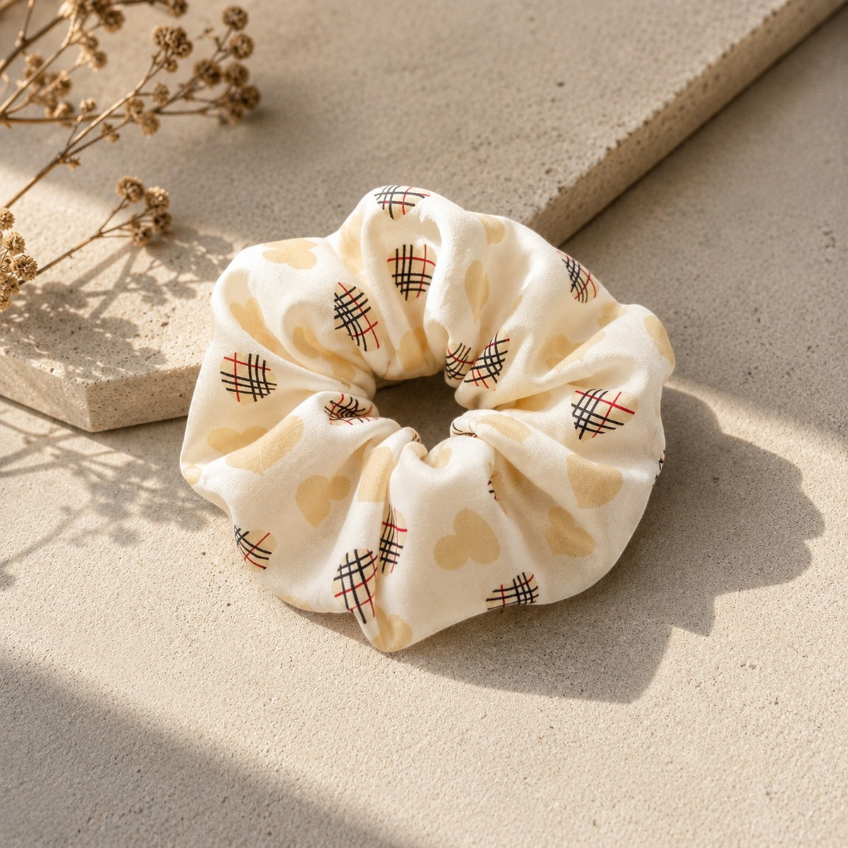 Second Soie jumbo scrunchie in cream fabric with Burberry-inspired heart and check patterns on a stone surface.