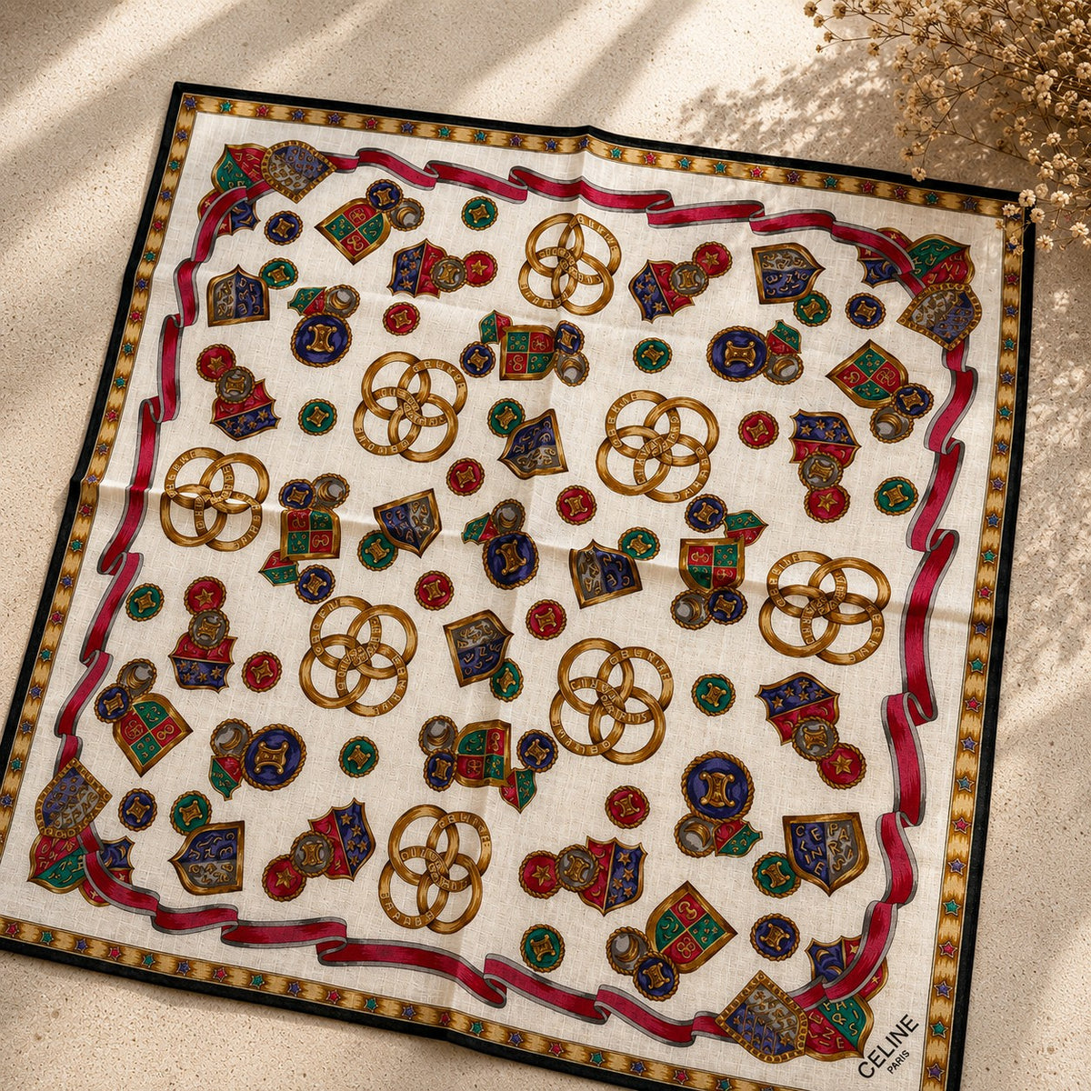 Second Soie vintage Celine handkerchief with cream background, red ribbons, and gold crest motifs on a textured surface.
