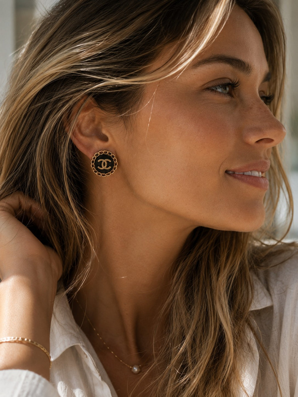 Second Soie vintage Chanel button earrings with black enamel, gold CC logo, and chain border worn by a woman.