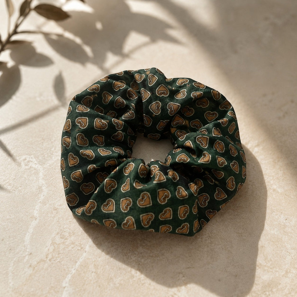 Second Soie vintage Moschino scrunchie in forest green silk with golden-brown heart print on a neutral stone surface.