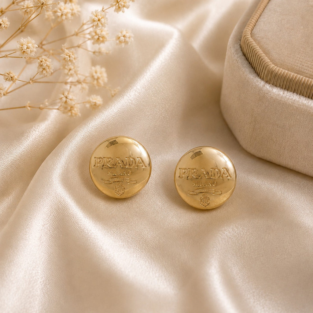 Second Soie vintage Prada Milano gold button earrings with a polished finish resting on cream satin fabric.