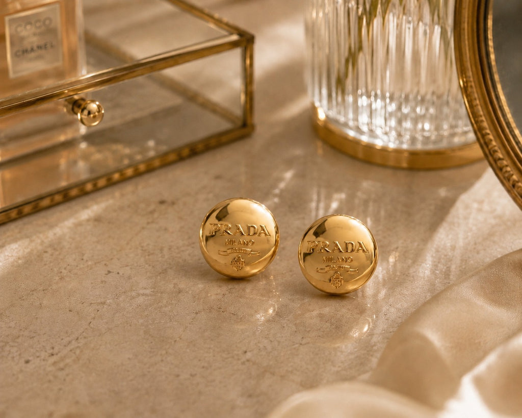 Second Soie vintage Prada Milano gold button earrings with a polished finish on a marble surface.